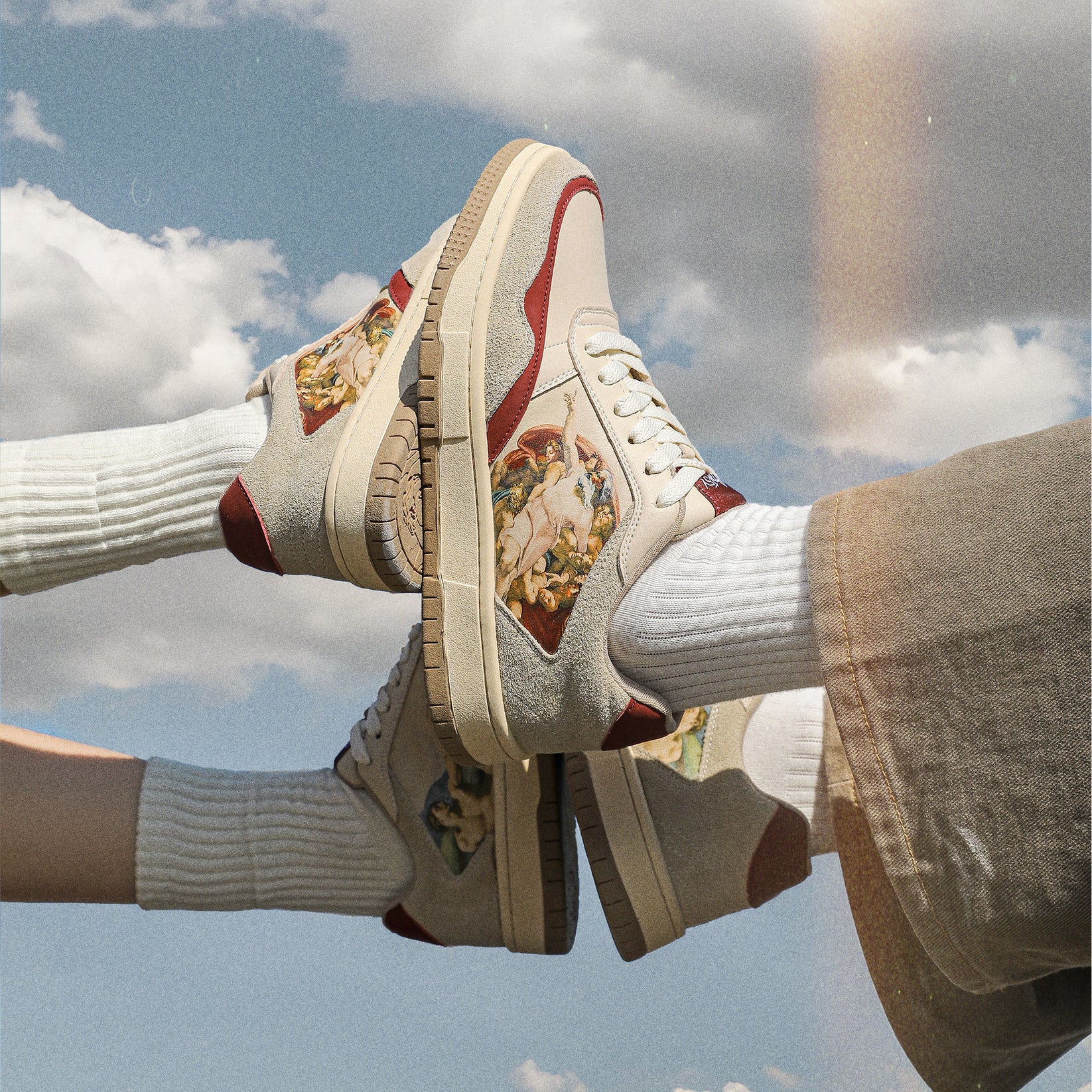 Two feet wearing artistic sneakers against a blue sky with clouds.
